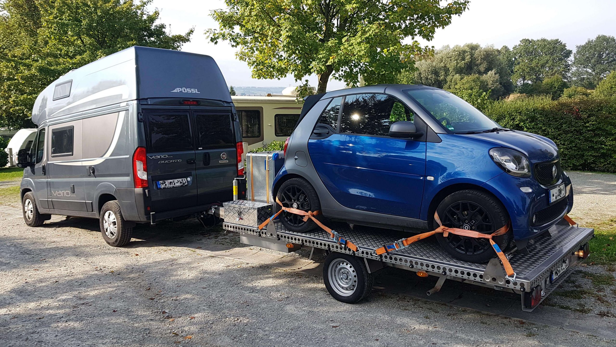 Smart und Staubox auf Edelstahl Einachs- Plattformanhänger auf einem Parkplatz