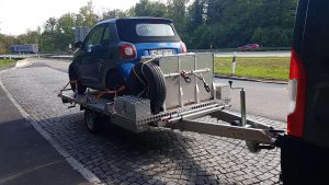 Smart und Staubox auf Edelstahl Einachs- Plattformanhänger auf einem Parkplatz