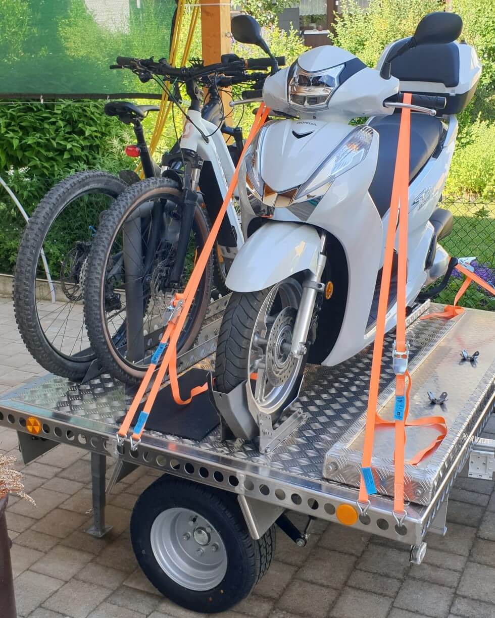 Zwei Fahrräder und ein Roller auf einem Aluminium Plattformanhänger - in einem Hof - von der Seite