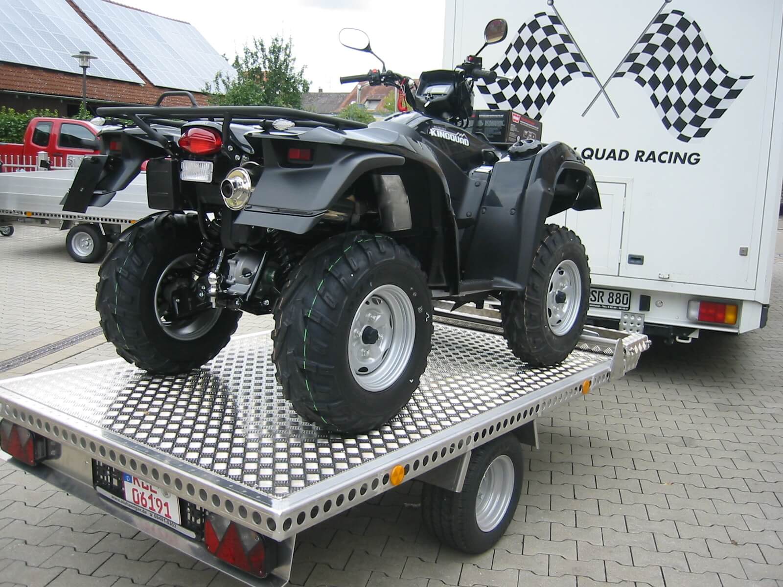 Schwarzes Quad auf Aluminium Anhänger hinter einem Wohnmobil - von hinten