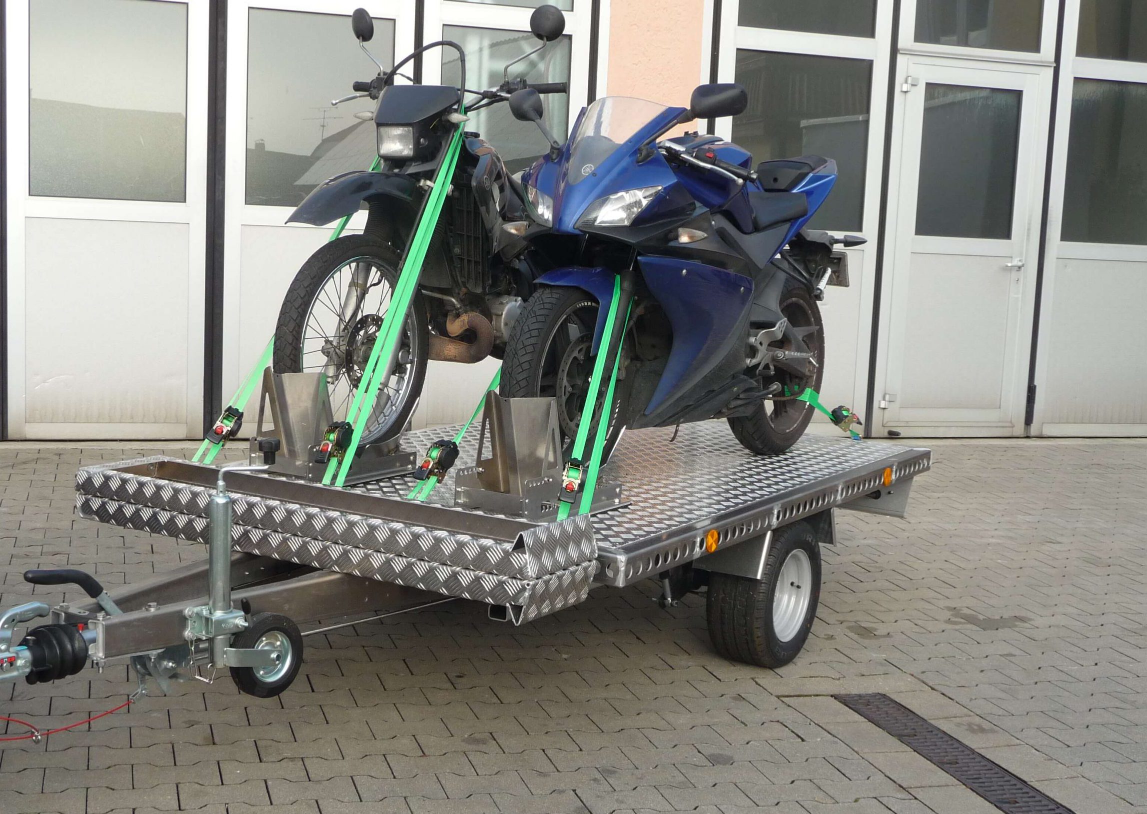 Zwei Motorräder auf einem Aluminium Plattformanhänger vor einem Hallentor - von vorne
