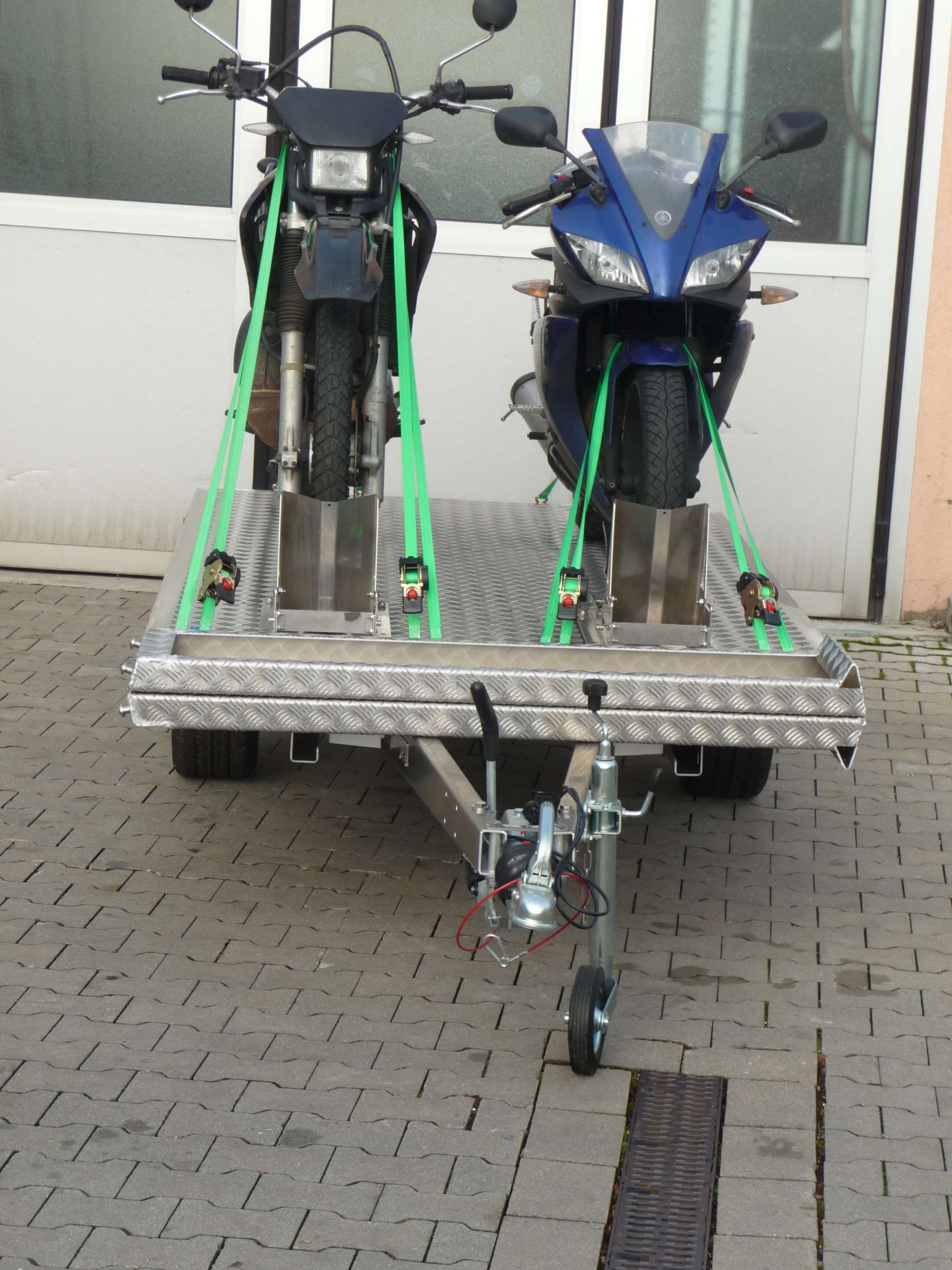 Zwei Motorräder auf einem Aluminium Plattformanhänger vor einem Hallentor - von vorne