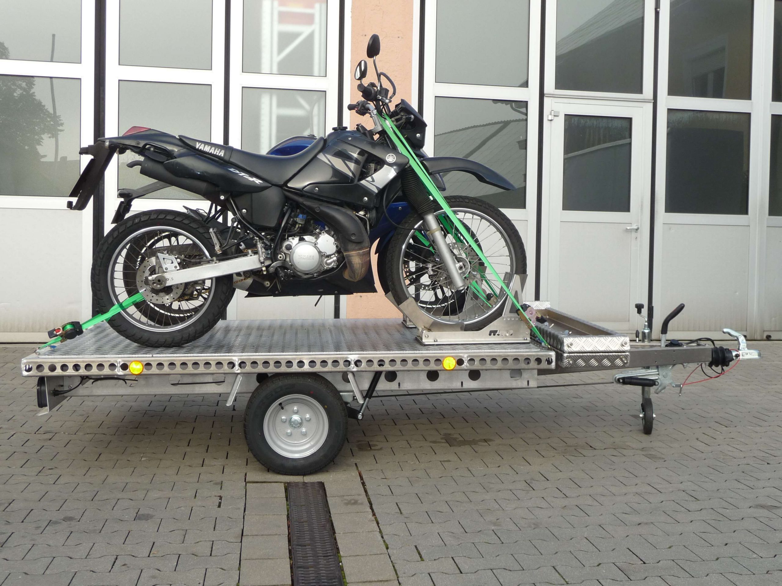 Zwei Motorräder auf einem Aluminium Plattformanhänger vor einem Hallentor - von der Seite