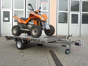 Oranges Quad auf Aluminium Anhänger vor einem Hallentor - von der Seite
