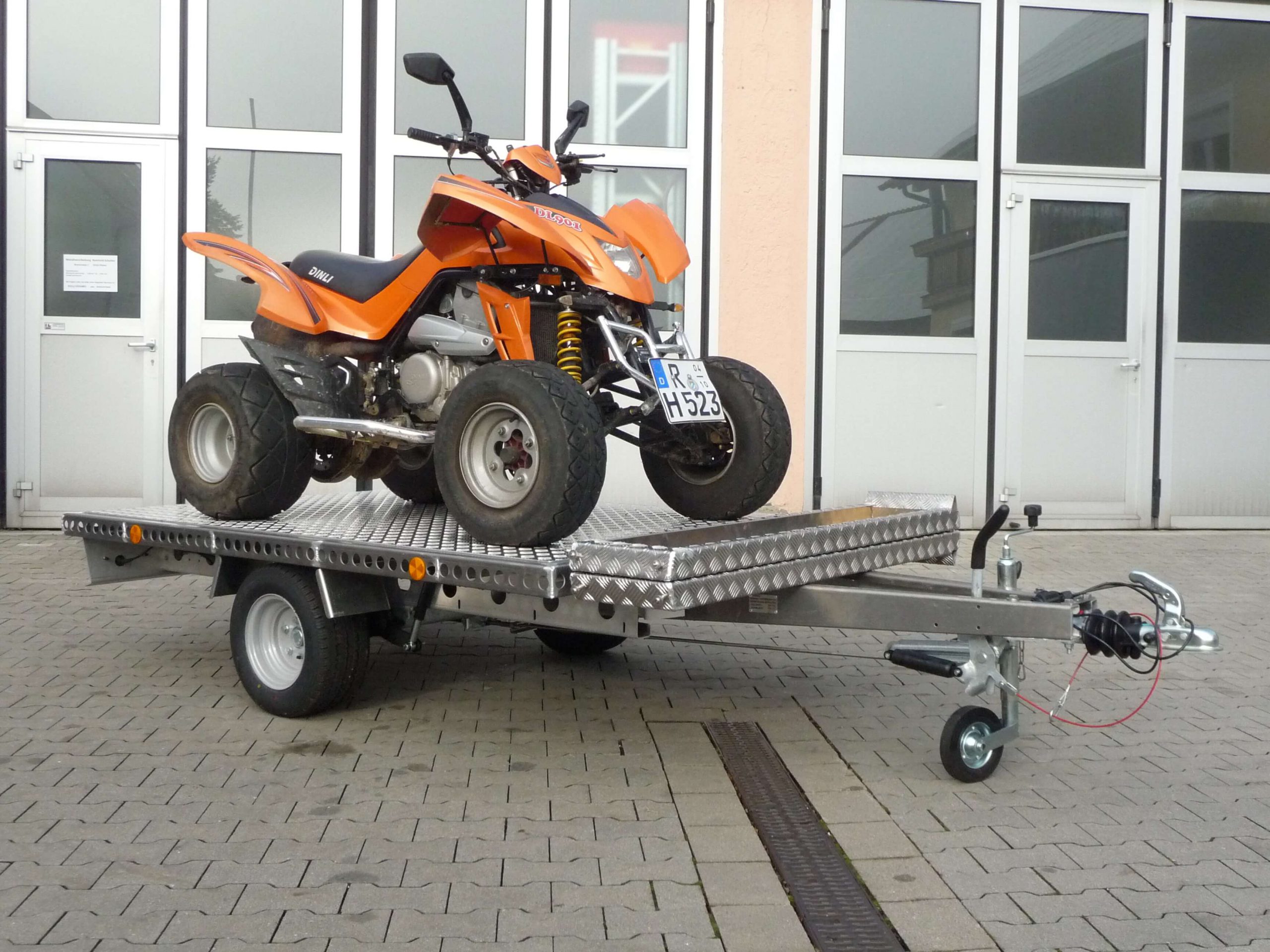 Oranges Quad auf Aluminium Anhänger vor einem Hallentor - von der Seite