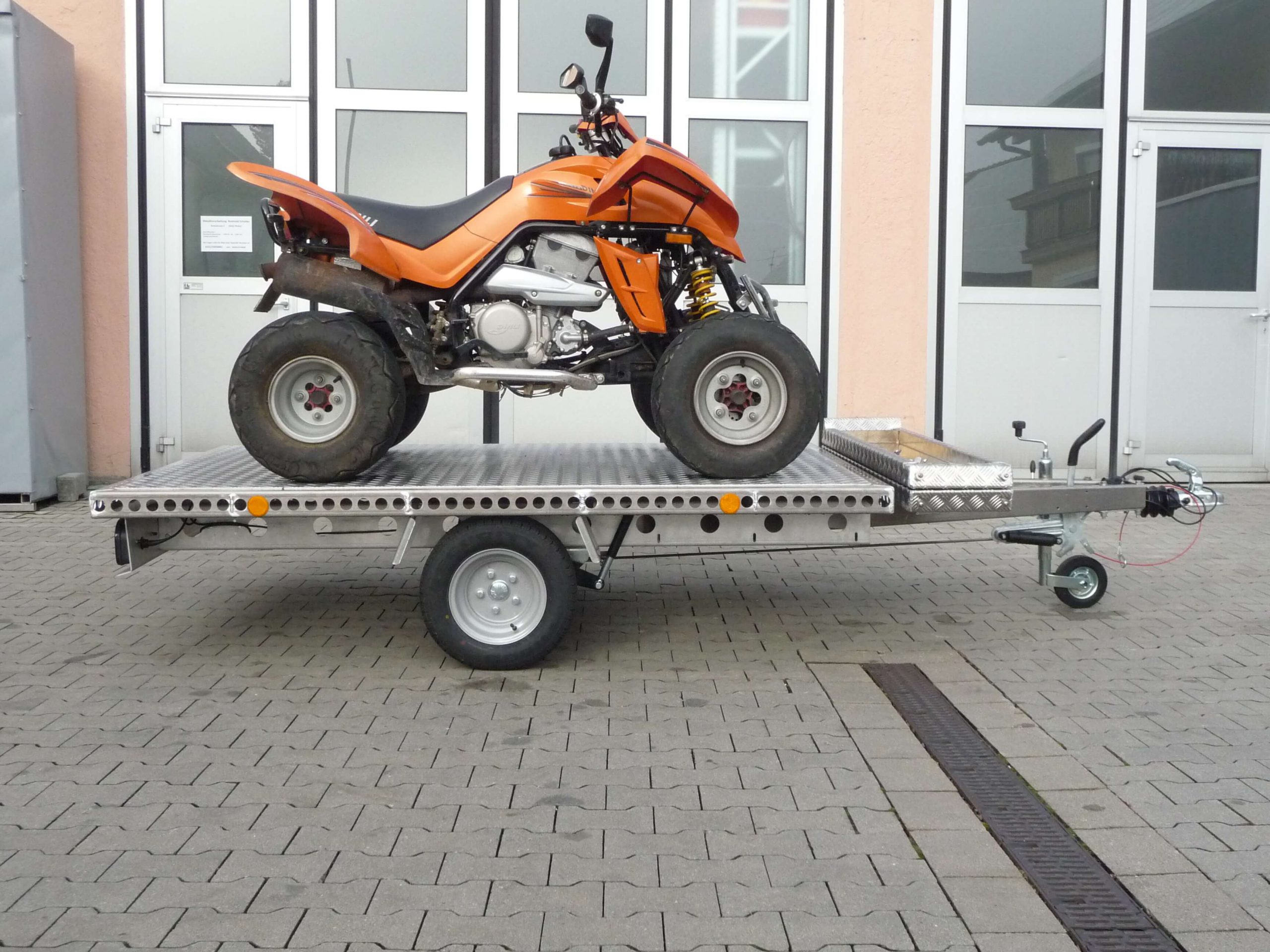 Oranges Quad auf Aluminium Anhänger vor einem Hallentor - von der Seite