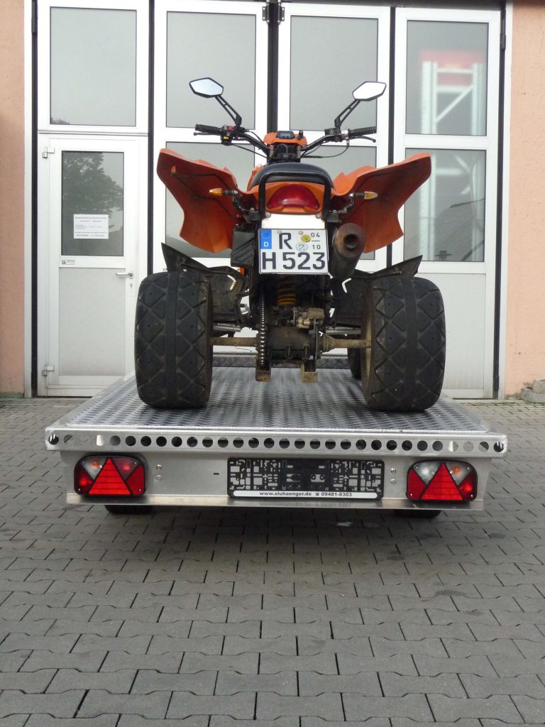 Oranges Quad auf Aluminium Anhänger vor einem Hallentor - von hinten
