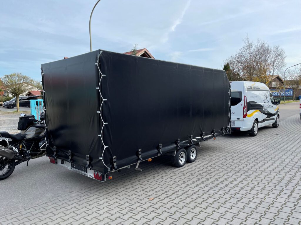 Anhänger mit Hochplane in schwarz mit Motorrad im Hof