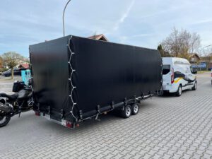 Anhänger mit Hochplane in schwarz mit Motorrad im Hof
