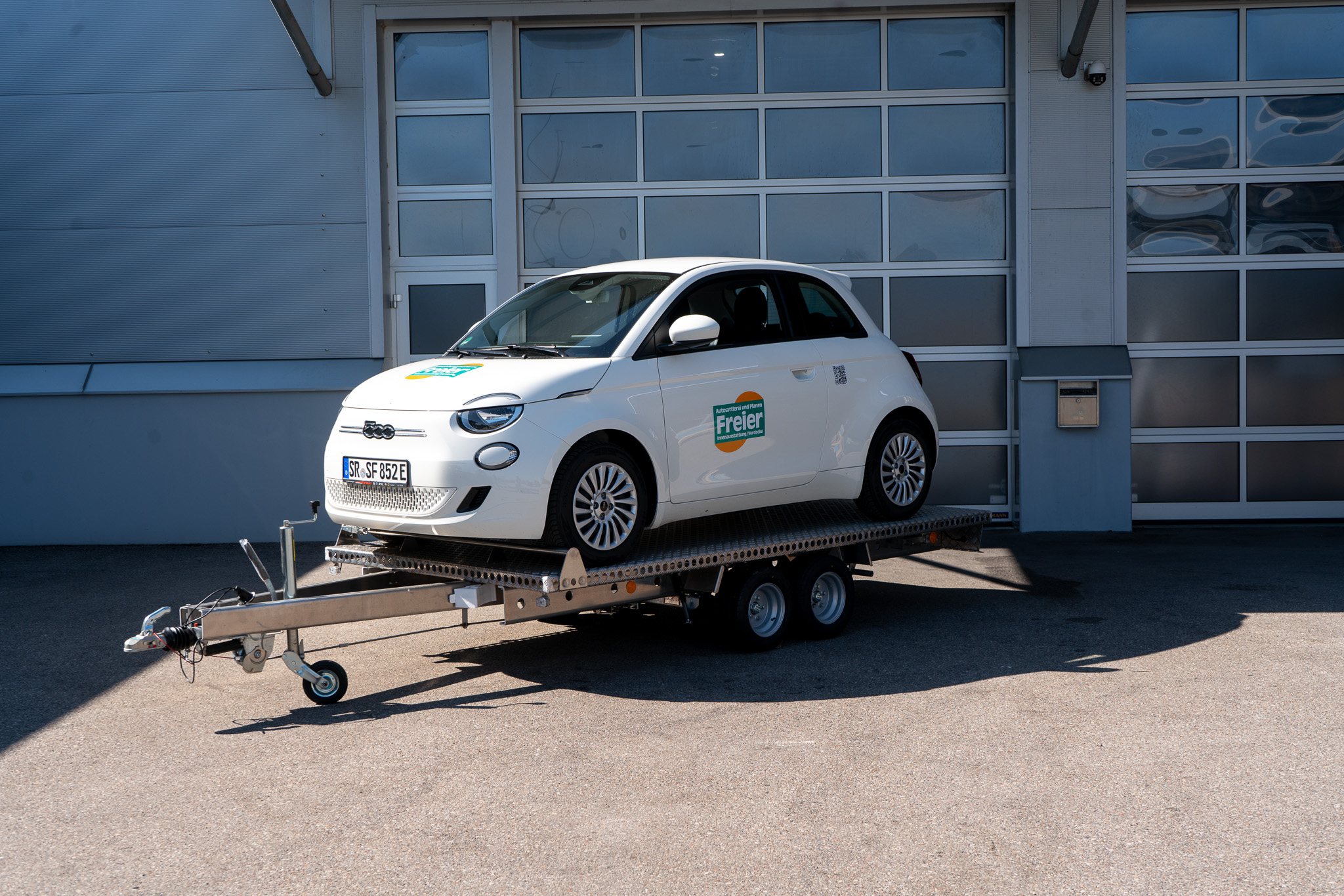 Aluminium Plattformanhänger Tandem, beladen mit einem weißen Fiat 500 vor einem Hallentor - Front