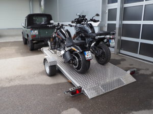 Zwei Motorräder auf einem abgesenkten Absenkanhänger verladen von hinten in einem Hof
