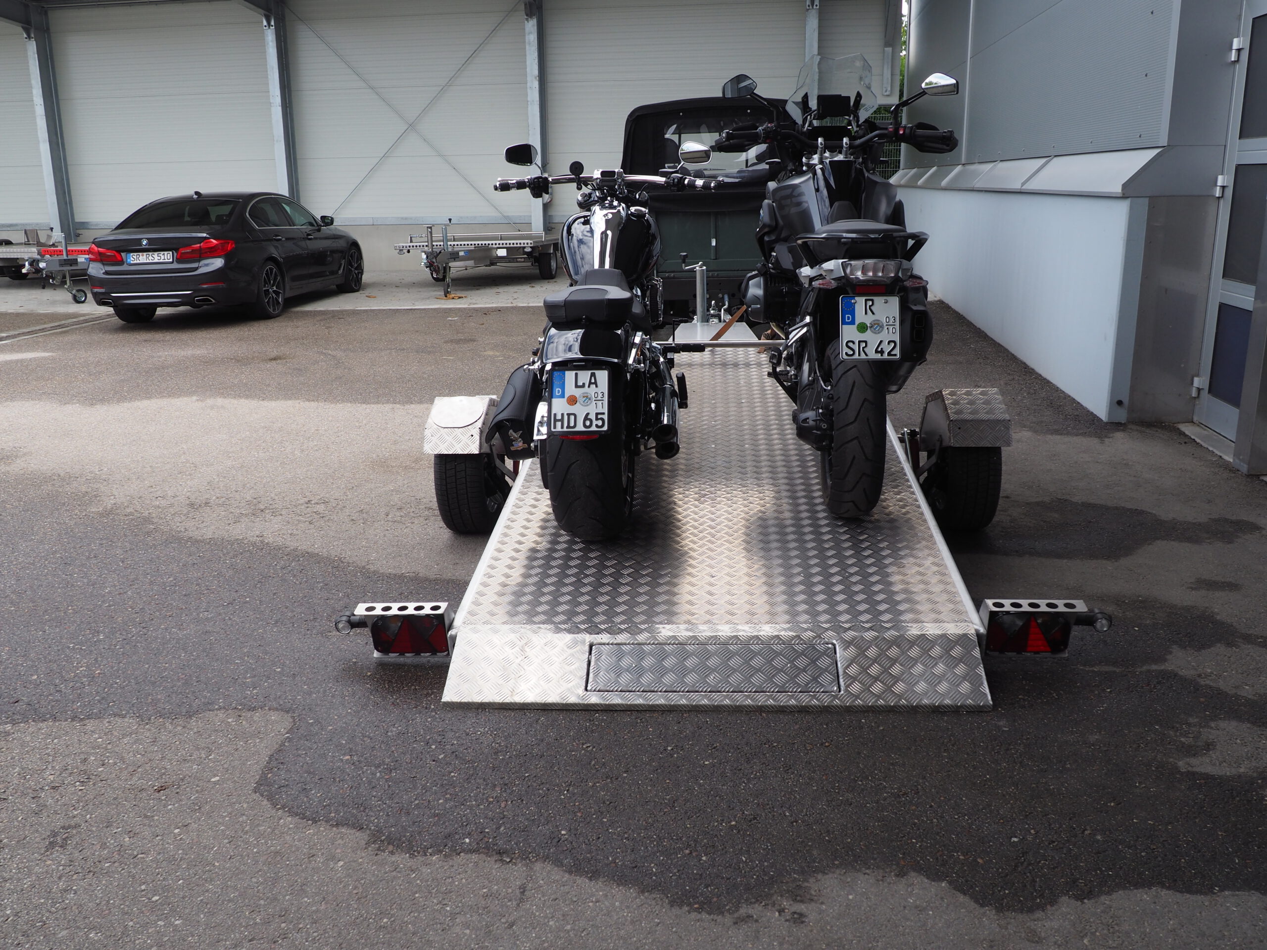 Zwei Motorräder auf einem abgesenkten Absenkanhänger verladen von hinten in einem Hof