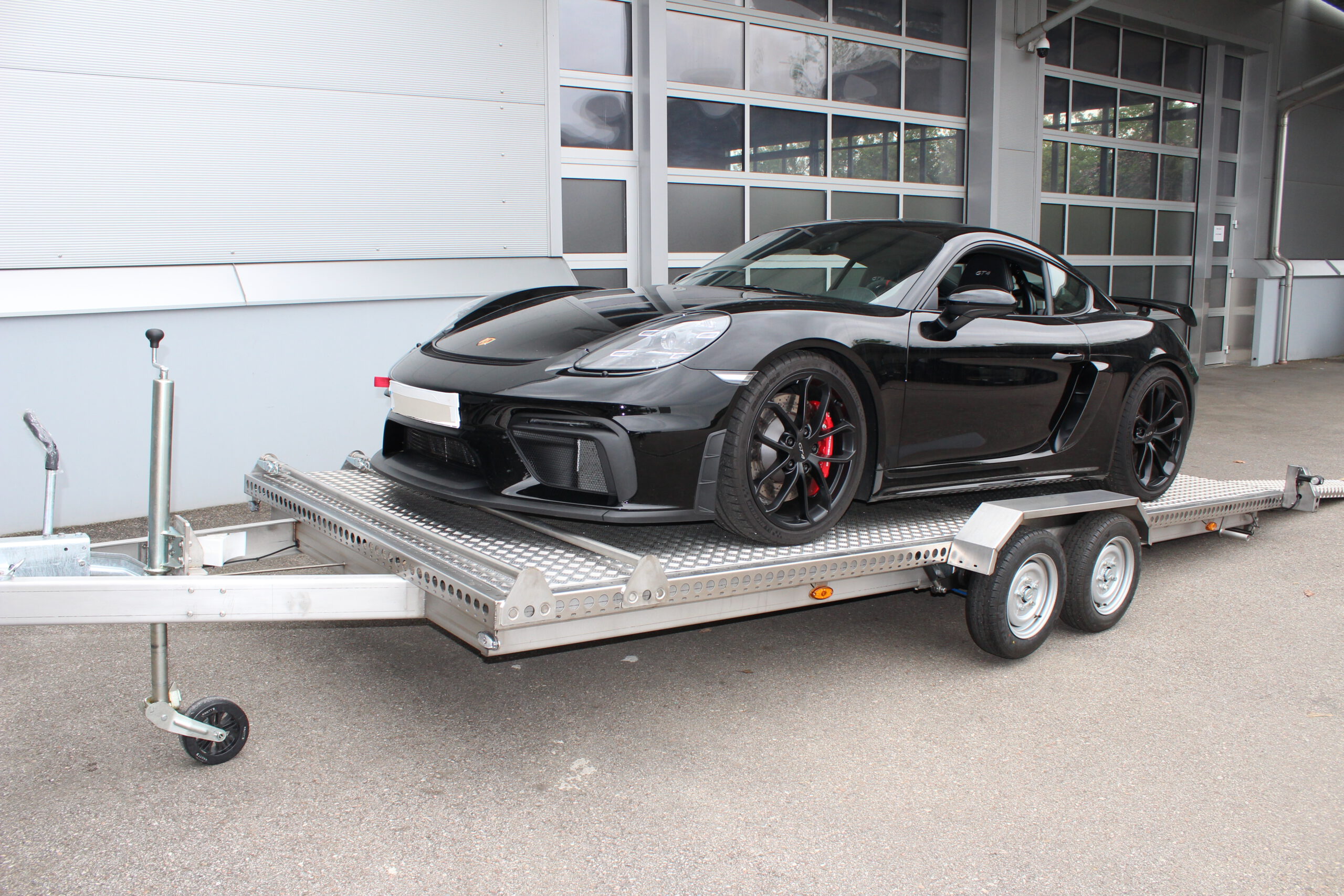 Porsche GT4 verladen auf Edelstahl Tieflader Anhänger - Ansicht von der Seite - vor Hallentor