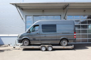 Mercedes Sprinter auf Edelstahl Tiefladeranhänger - Ansicht von der Seite vor einem Hallentor