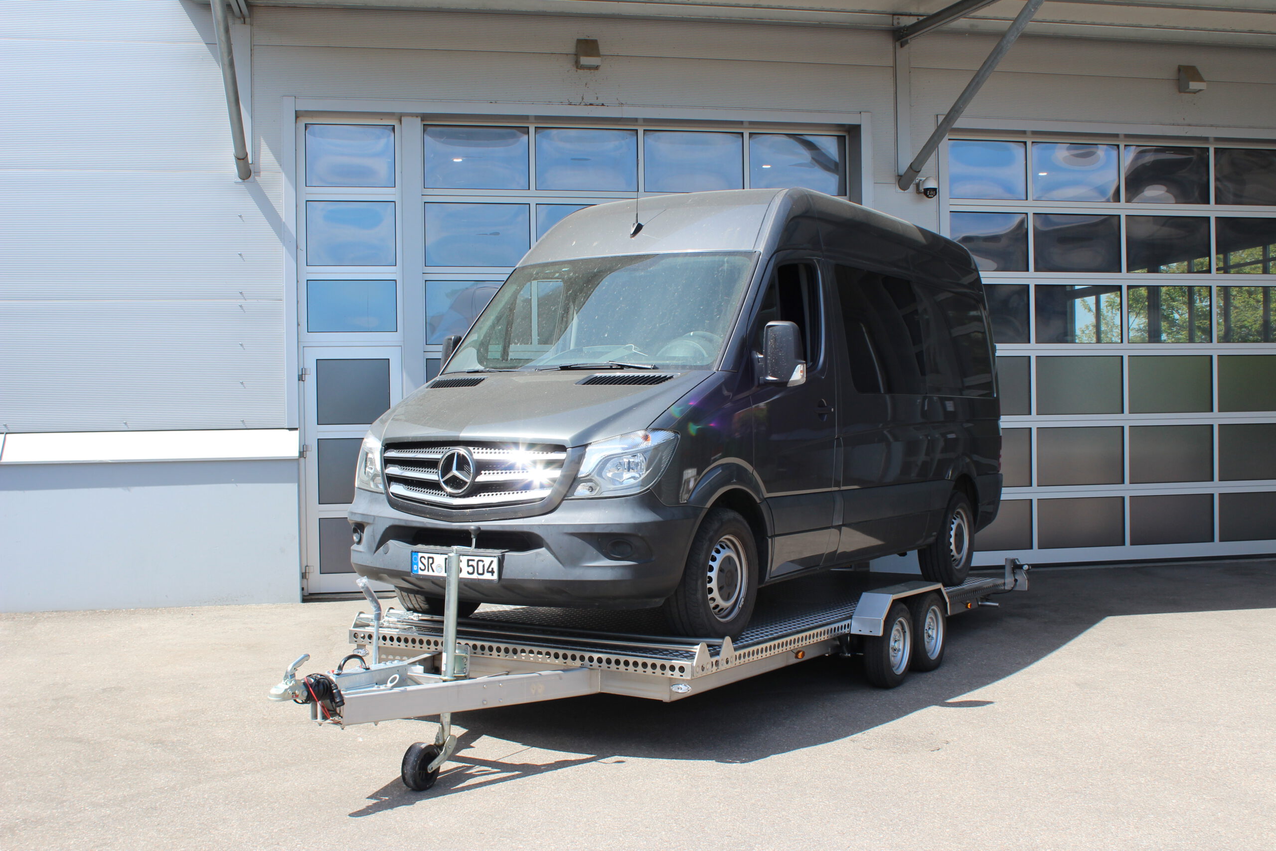 Mercedes Sprinter auf Edelstahl Tiefladeranhänger - Ansicht von vorne vor einem Hallentor