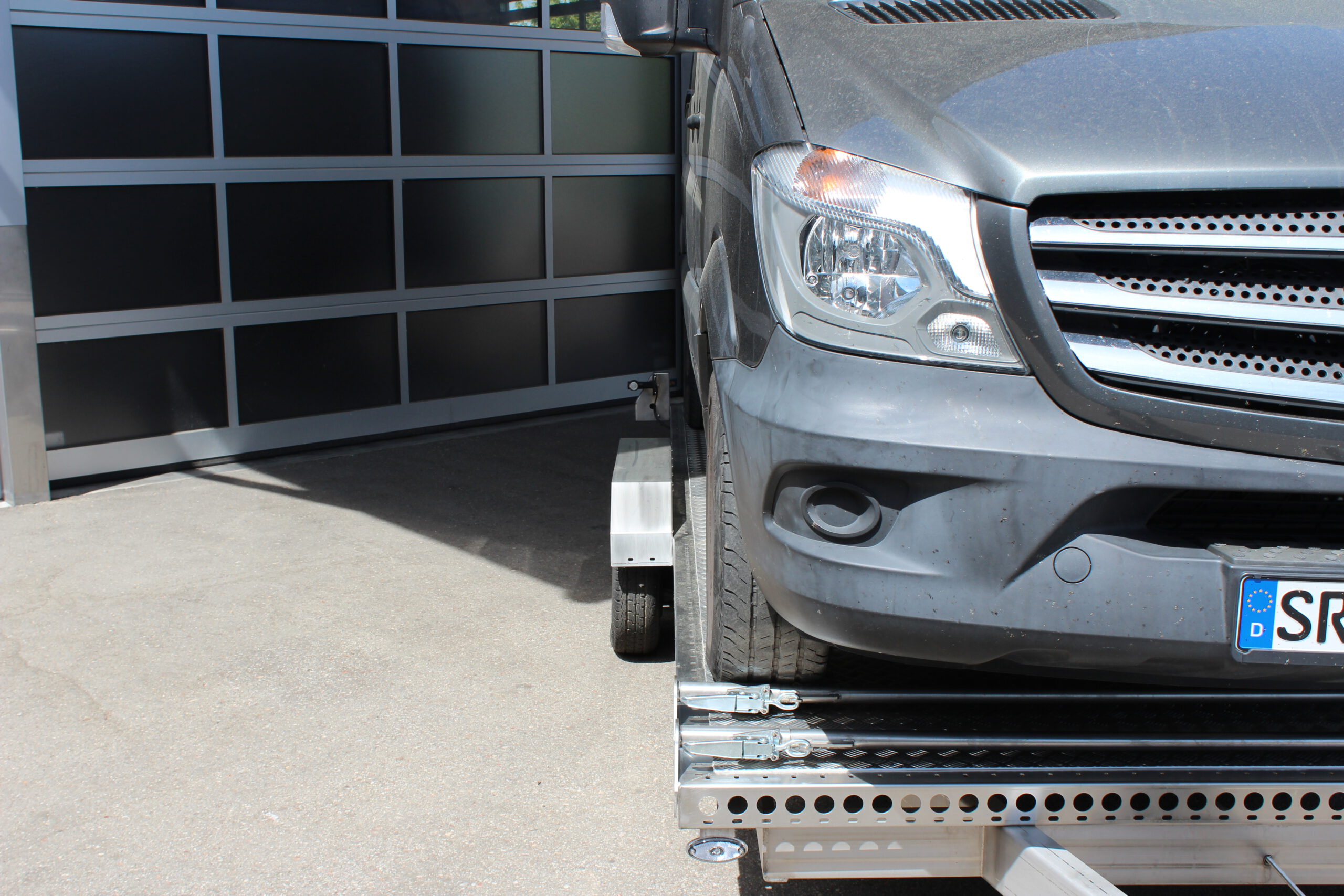 Mercedes Sprinter auf Edelstahl Tiefladeranhänger - Detailaufnahme Beifahrerseite von vorne vor einem Hallentor