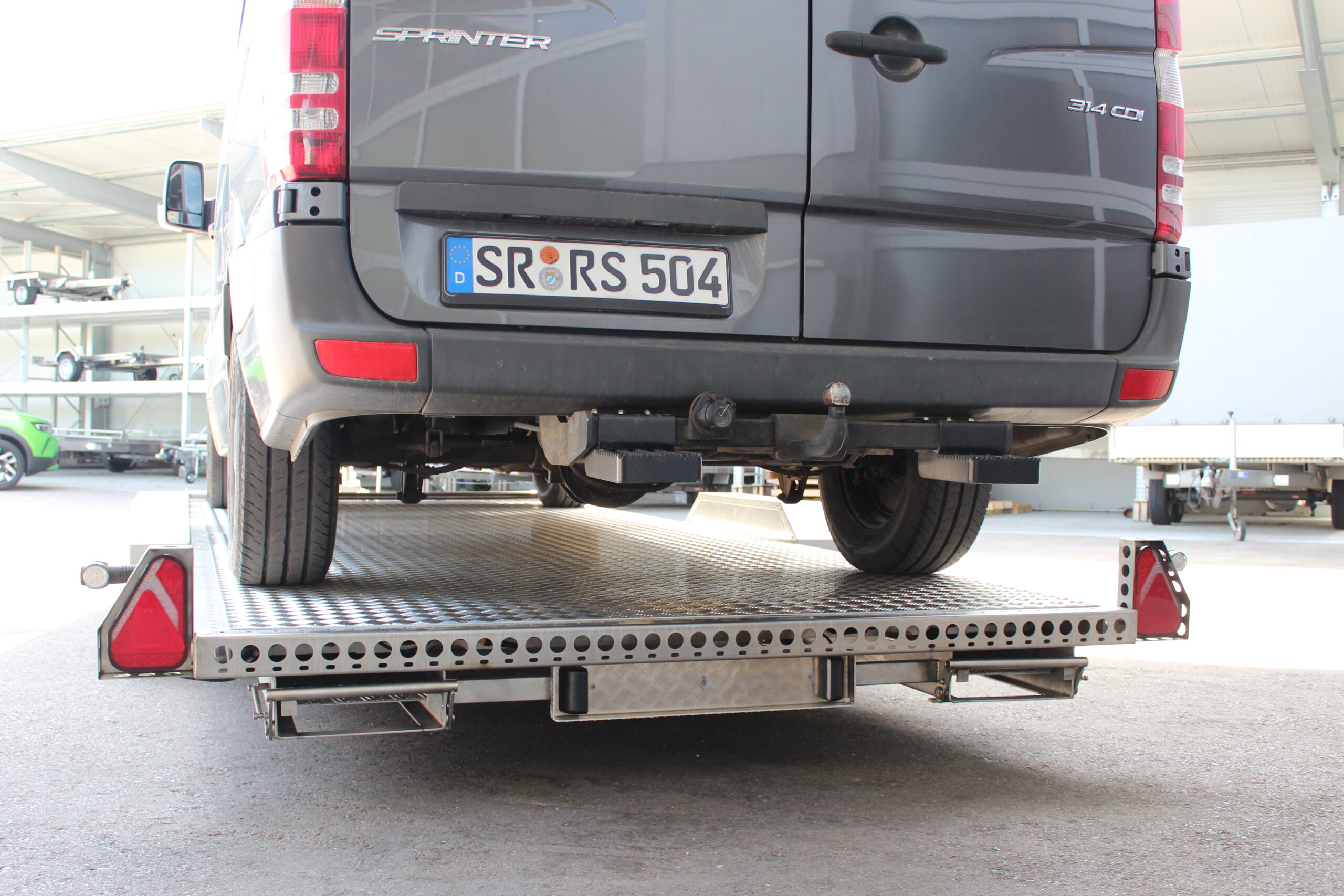 Mercedes Sprinter auf Edelstahl Tiefladeranhänger - Ansicht von hinten in einem Hof
