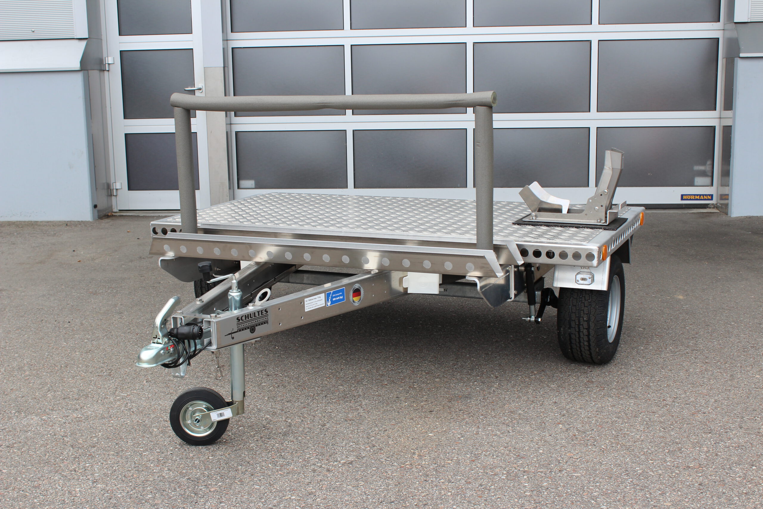 Kleiner Aluminium Plattformanhänger mit Radwippe und Fahrradträger - Frontansicht vor einem Hallentor