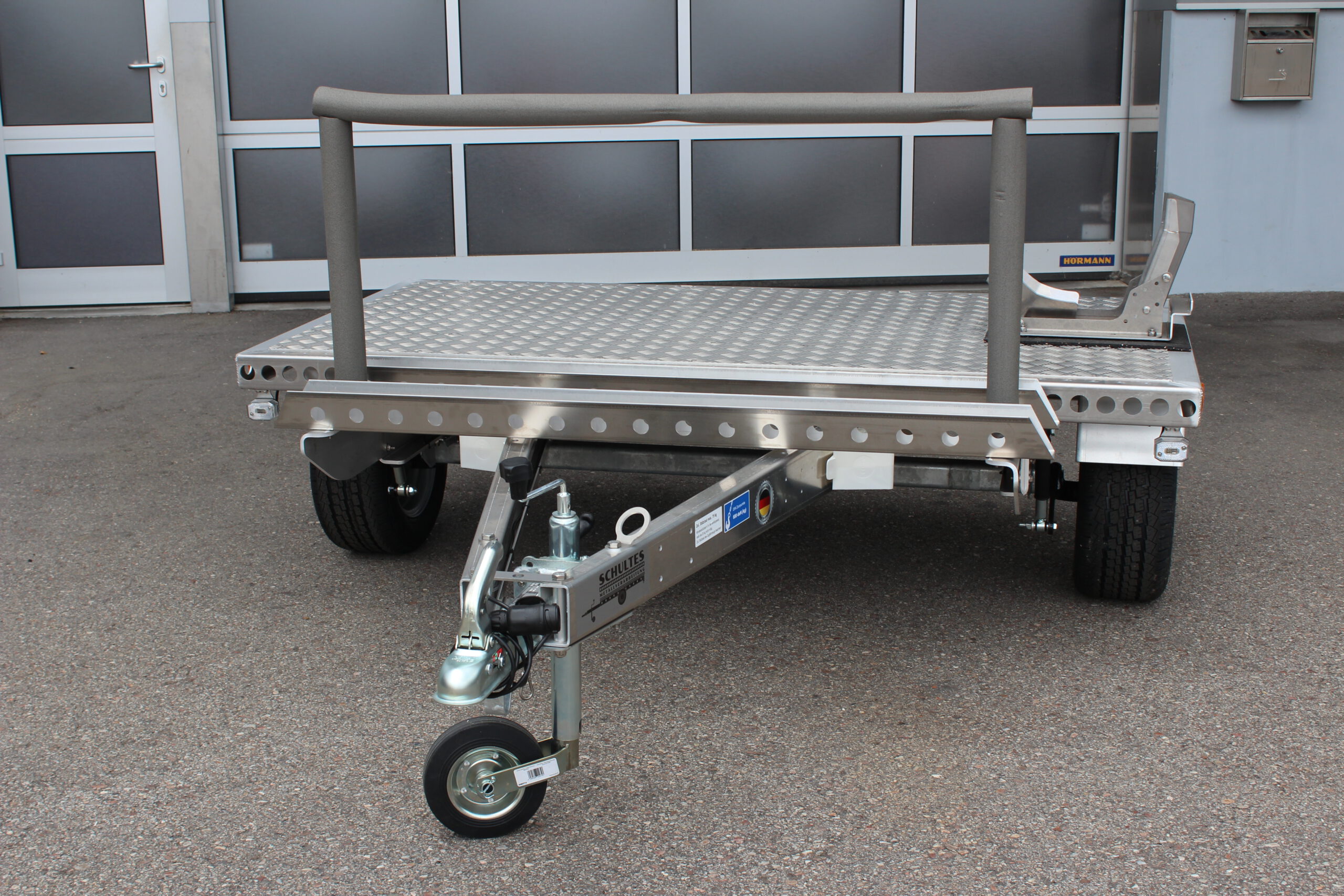 Kleiner Aluminium Plattformanhänger mit Radwippe und Fahrradträger - Frontansicht vor einem Hallentor