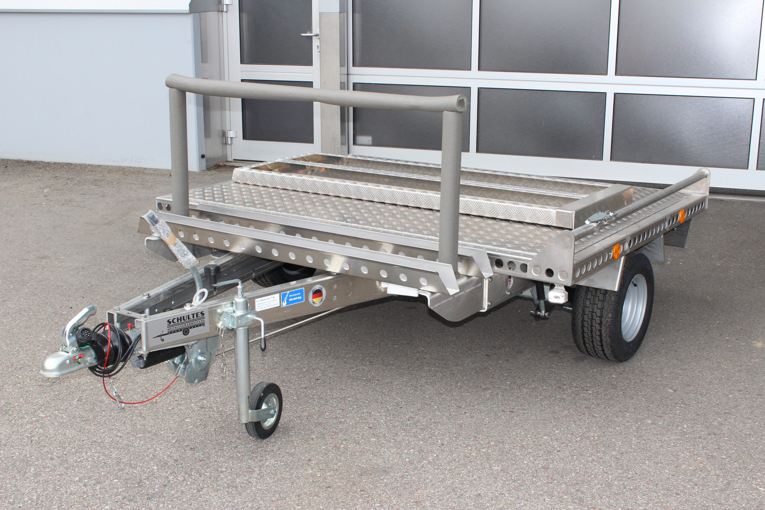 Kleiner Aluminium Plattformanhänger mit zwei Auffahrrampen und Fahrradträger - Ansicht von vorne vor einem Hallentor