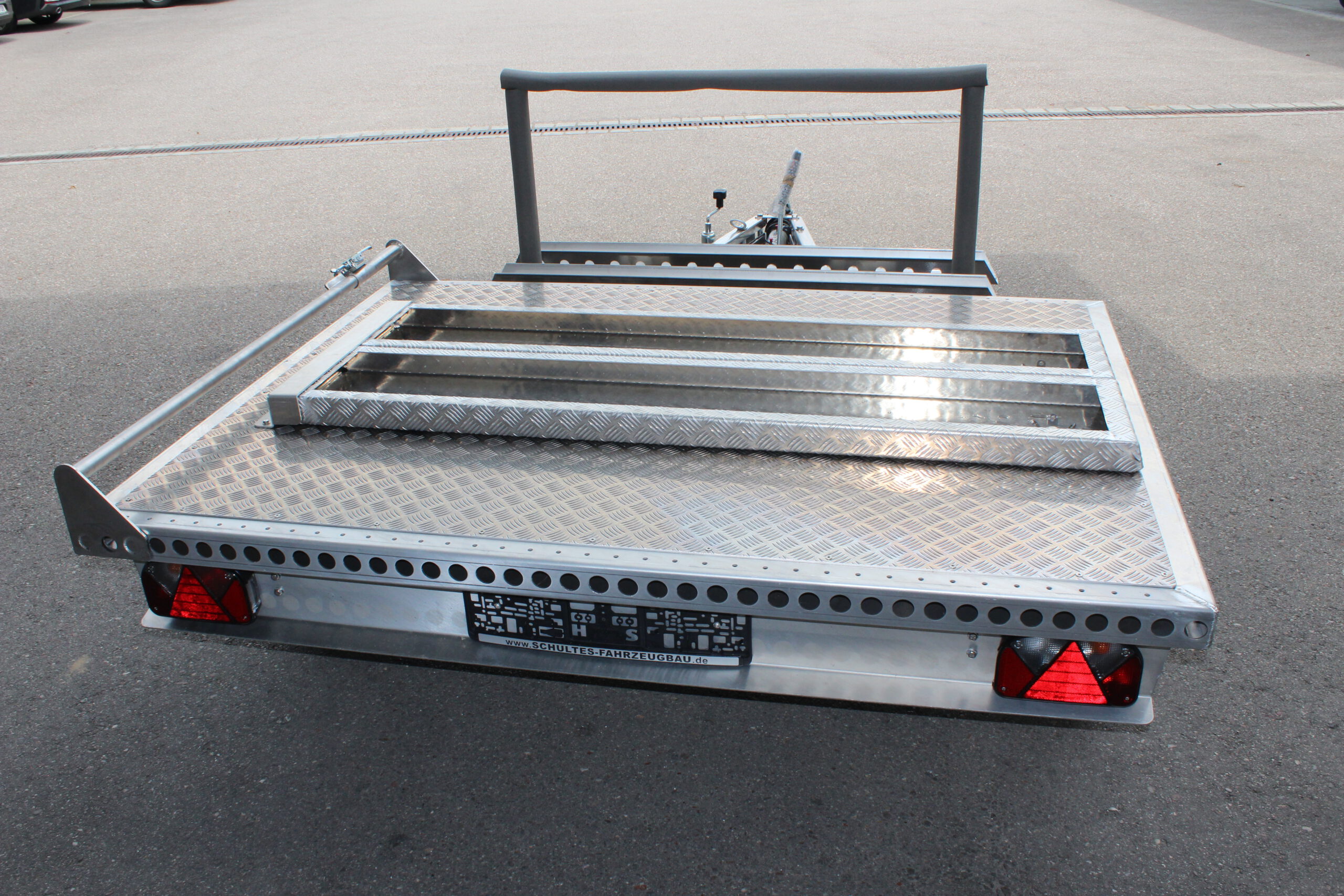 Kleiner Aluminium Plattformanhänger mit zwei Auffahrrampen und Fahrradträger - Ansicht von hinten in einem Hof
