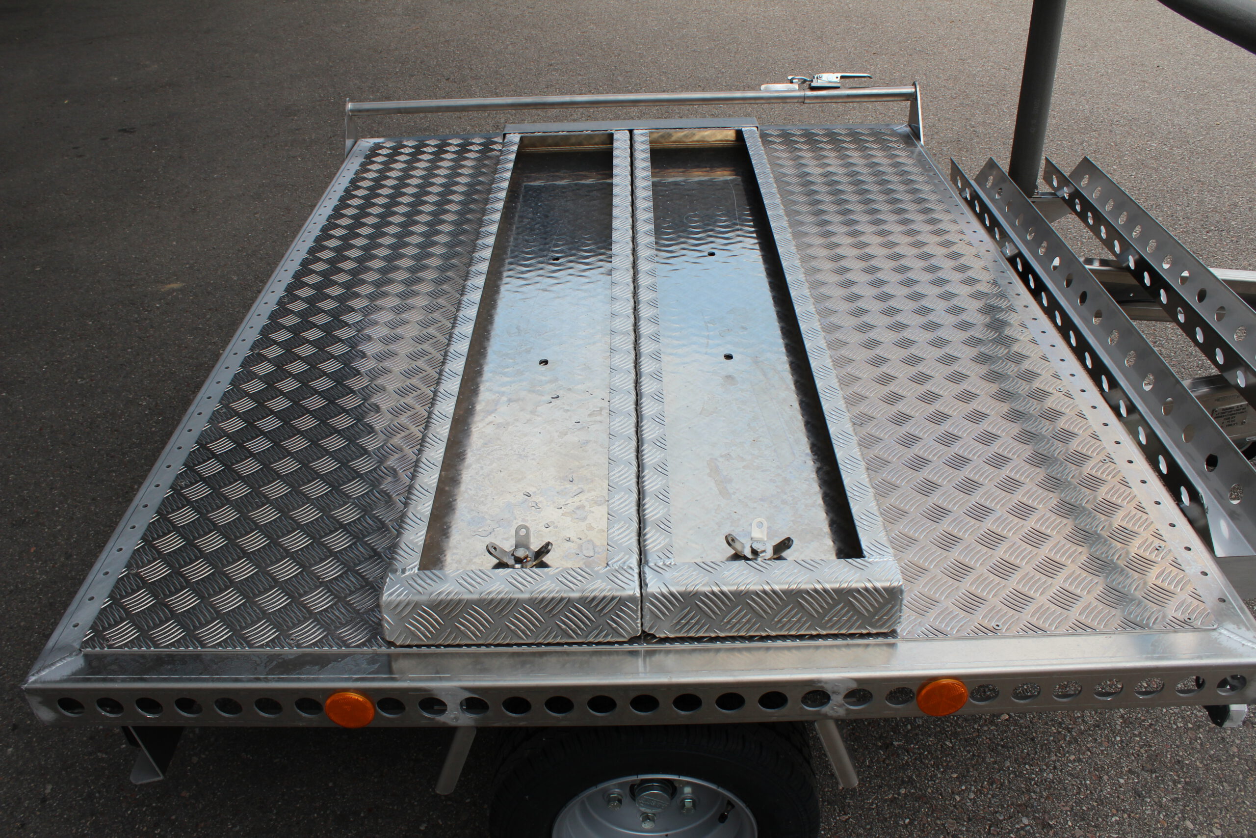Kleiner Aluminium Plattformanhänger mit zwei Auffahrrampen und Fahrradträger - Ansicht von der Seite in einem Hof
