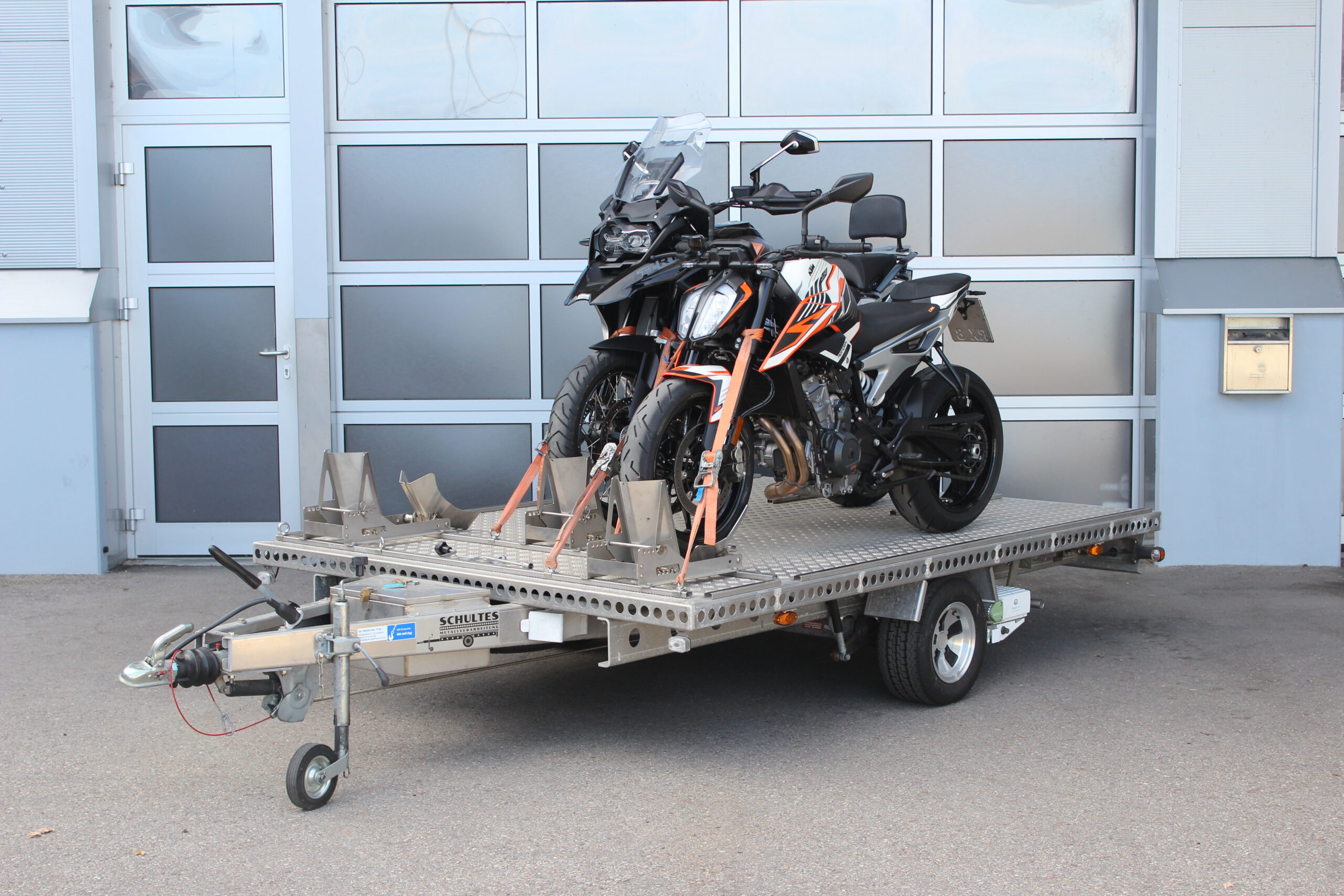 Aluminium Anhänger für drei Motorräder beladen mit BMW GS und KTM Duke vor einem Garagentor - Ansicht von Vorne