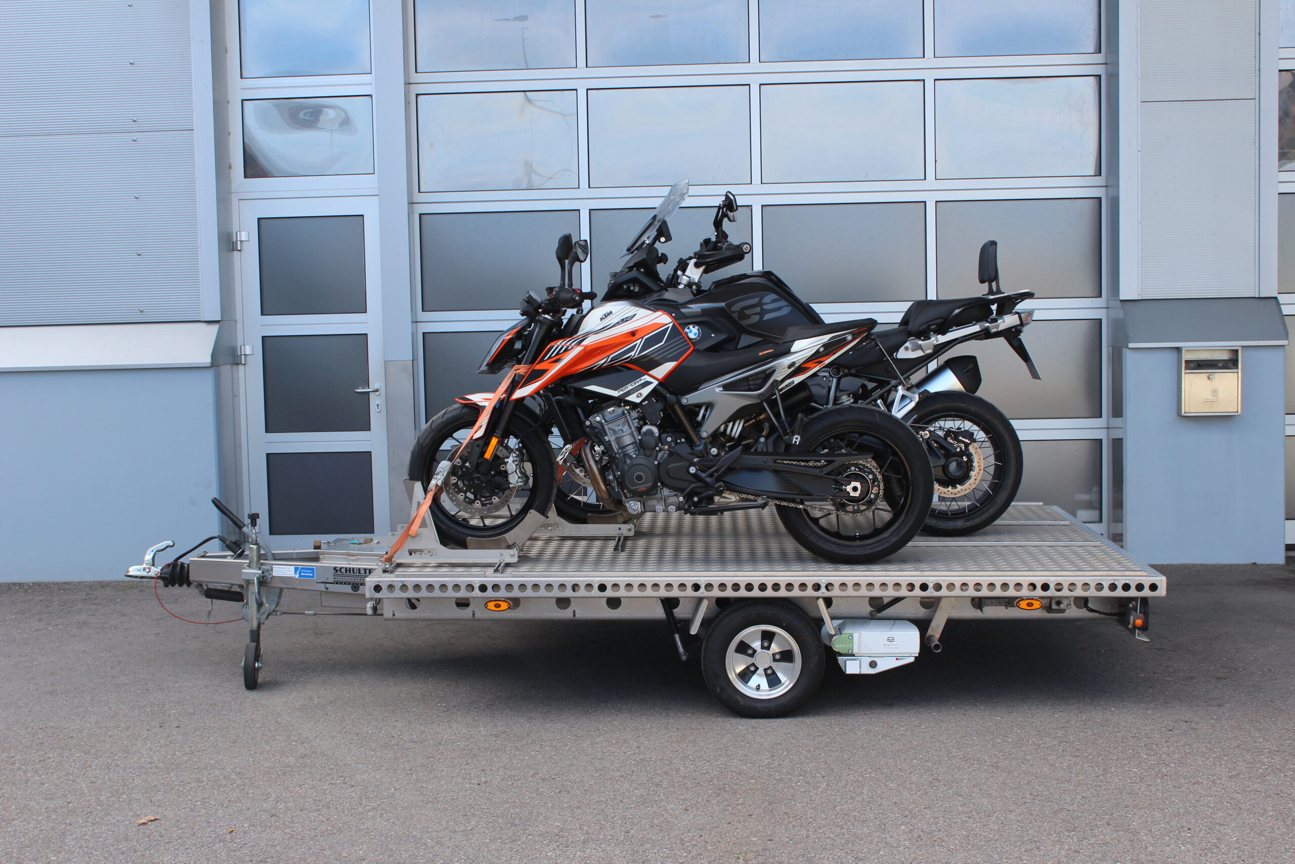 Aluminium Anhänger für drei Motorräder beladen mit BMW GS und KTM Duke vor einem Garagentor - Ansicht von der Seite