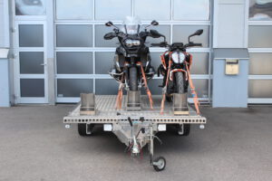 Aluminium Anhänger für drei Motorräder beladen mit BMW GS und KTM Duke vor einem Garagentor - Ansicht von Vorne