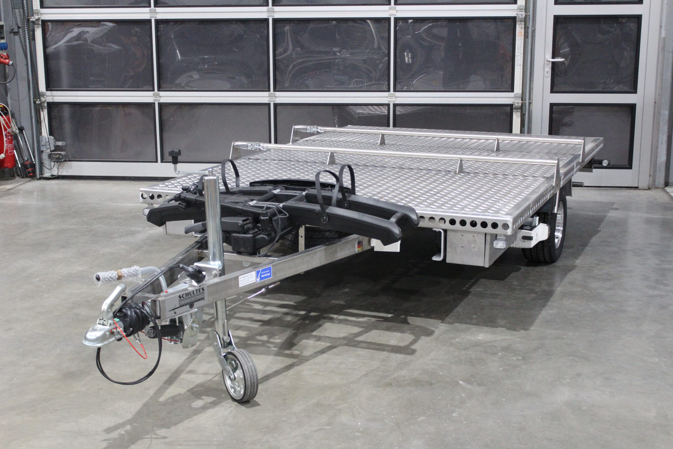 Aluminium Plattformanhänger mit verlängerter Zugdeichsel und Fahrradträger auf der Deichsel in einer Halle vor einem Tor