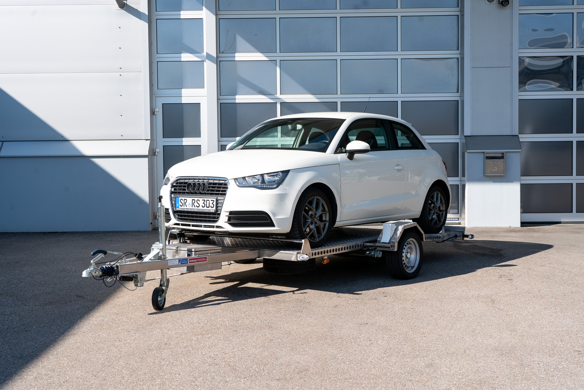 Edelstahl Absenkanhänger fertig beladen - Audi A1 steht auf dem Anhänger - vor einem Hallentor - Frontansicht