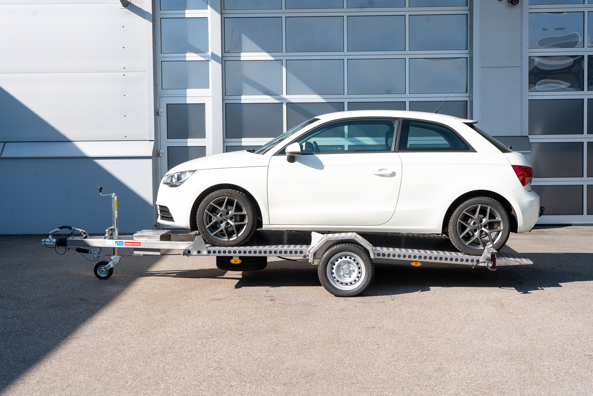 Edelstahl Absenkanhänger fertig beladen - Audi A1 steht auf dem Anhänger - vor einem Hallentor - Seitenansicht