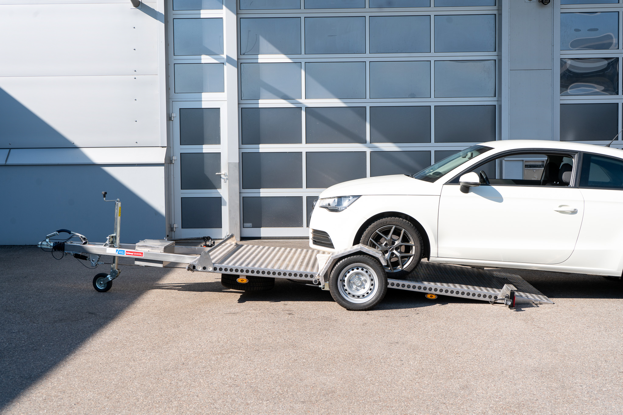 Edelstahl Absenkanhänger abgesenkt - Audi A1 steht halb auf dem Anhänger - vor einem Hallentor - Seitenansicht