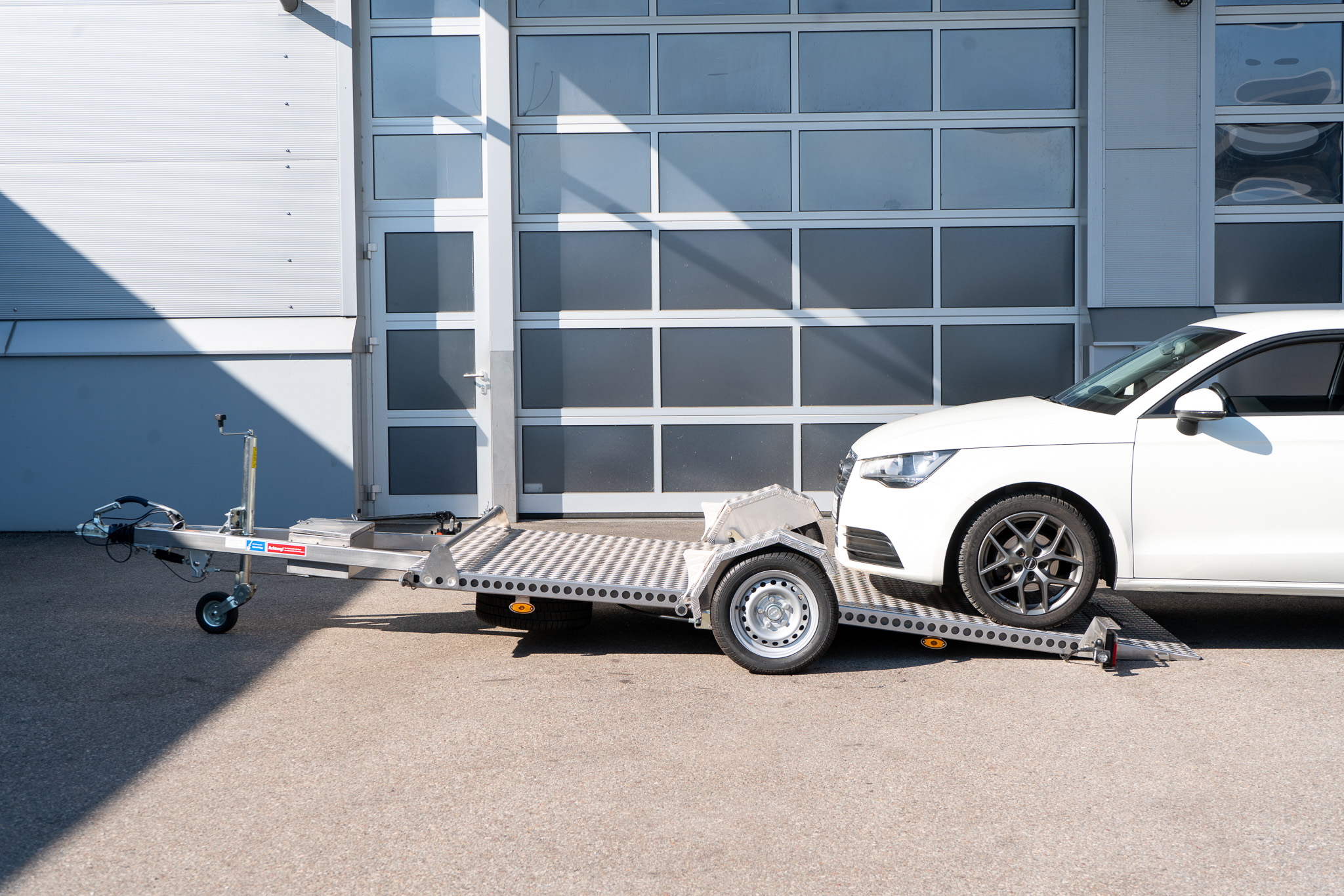 Edelstahl Absenkanhänger abgesenkt - Audi A1 steht halb auf dem Anhänger - vor einem Hallentor - Seitenansicht