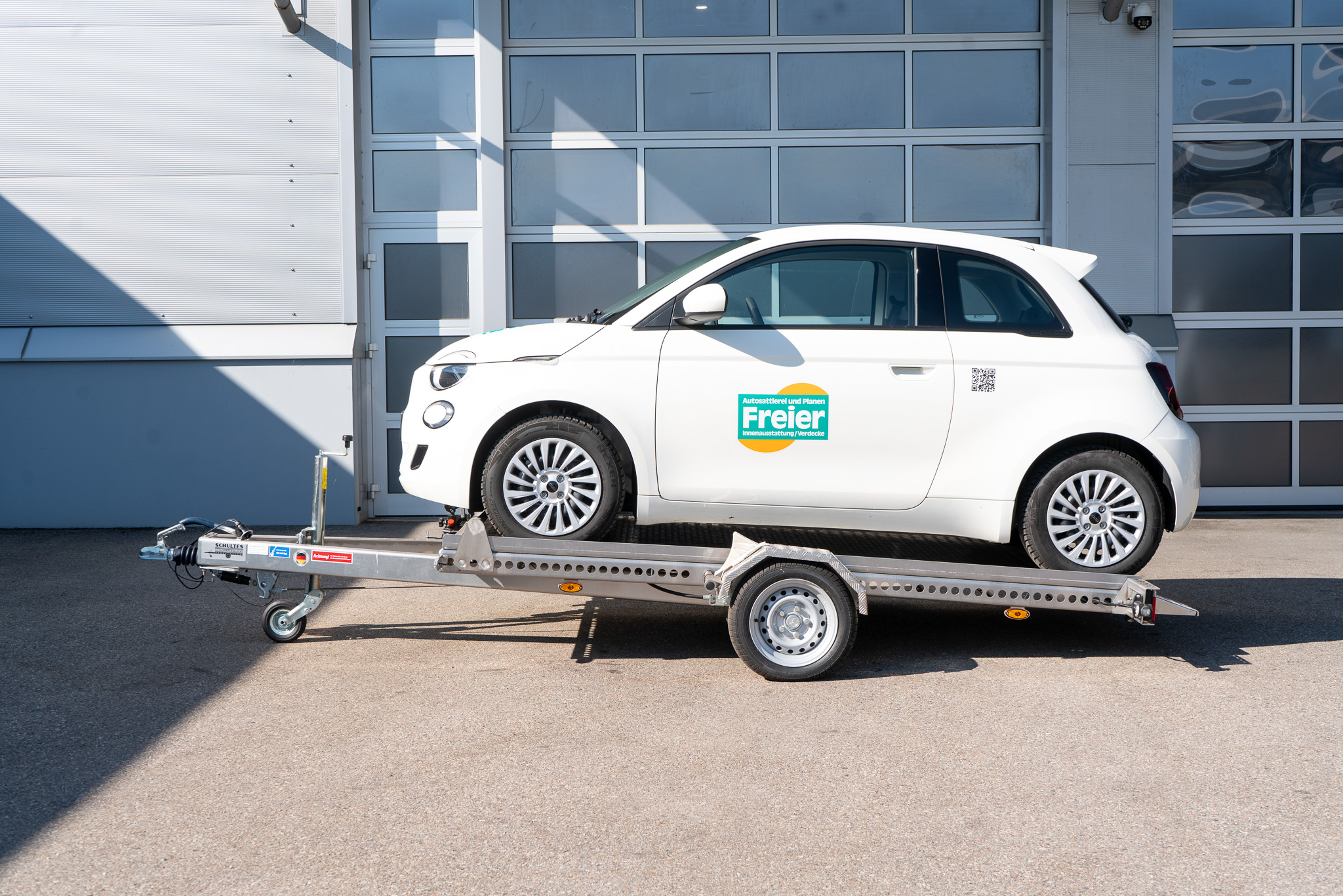 Absenkanhänger beladen mit weißem Fiat 500 auf dem Anhänger - Ansicht von der Seite vor einem geschlossenen Hallentor
