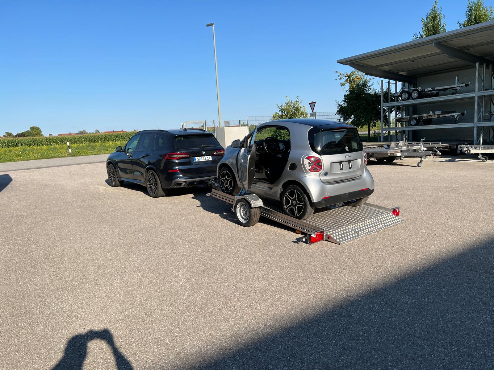 Smart fortwo auf abgesenktem Absenkanhänger hinter einem Auto in einem Hof