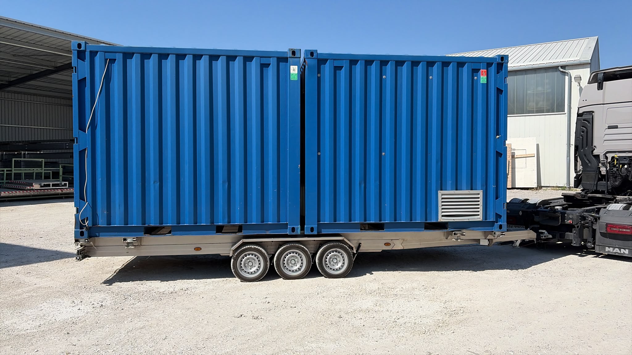Edelstahl Containertransport-Anhänger mit zwei blauen Containern beladen auf einem Hof hinter einem LKW
