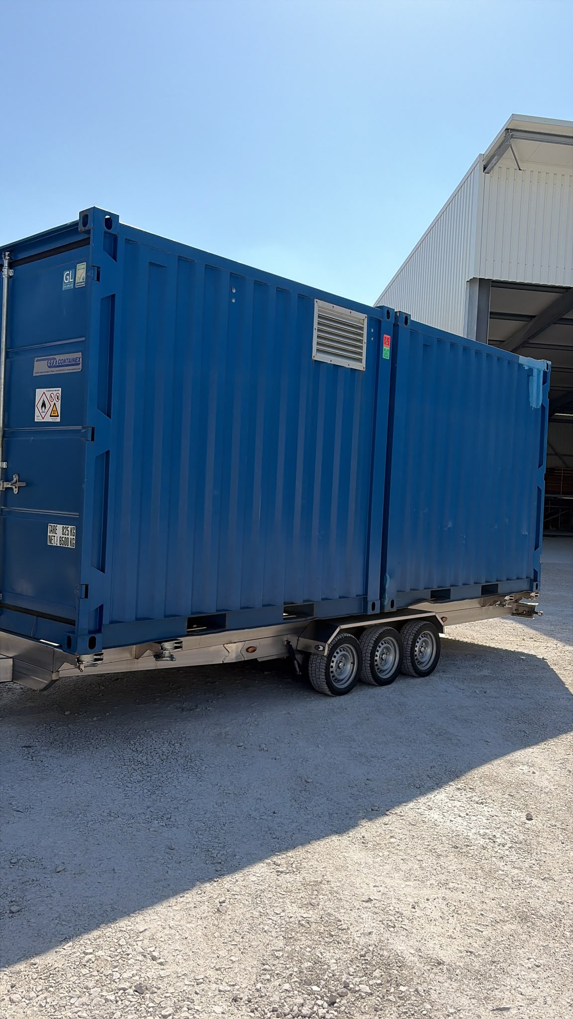 Edelstahl Containertransport-Anhänger mit zwei blauen Containern beladen auf einem Hof hinter einem LKW
