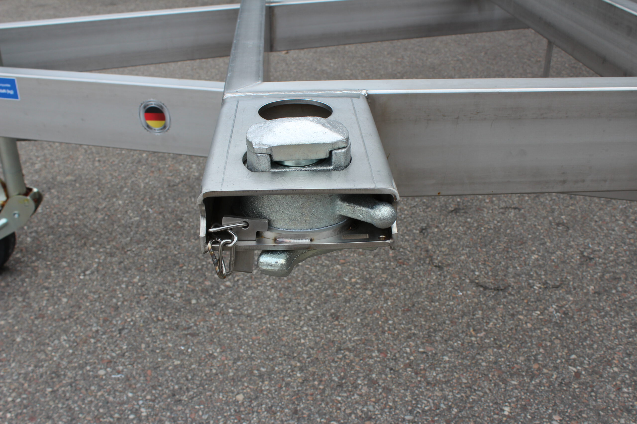 Anhänger aus Edelstahl zum Transport von Überseecontainern. Anhänger steht vor einem Hallentor. Anhängerfahrgestell ohne Bodenplatte für Containertransport.