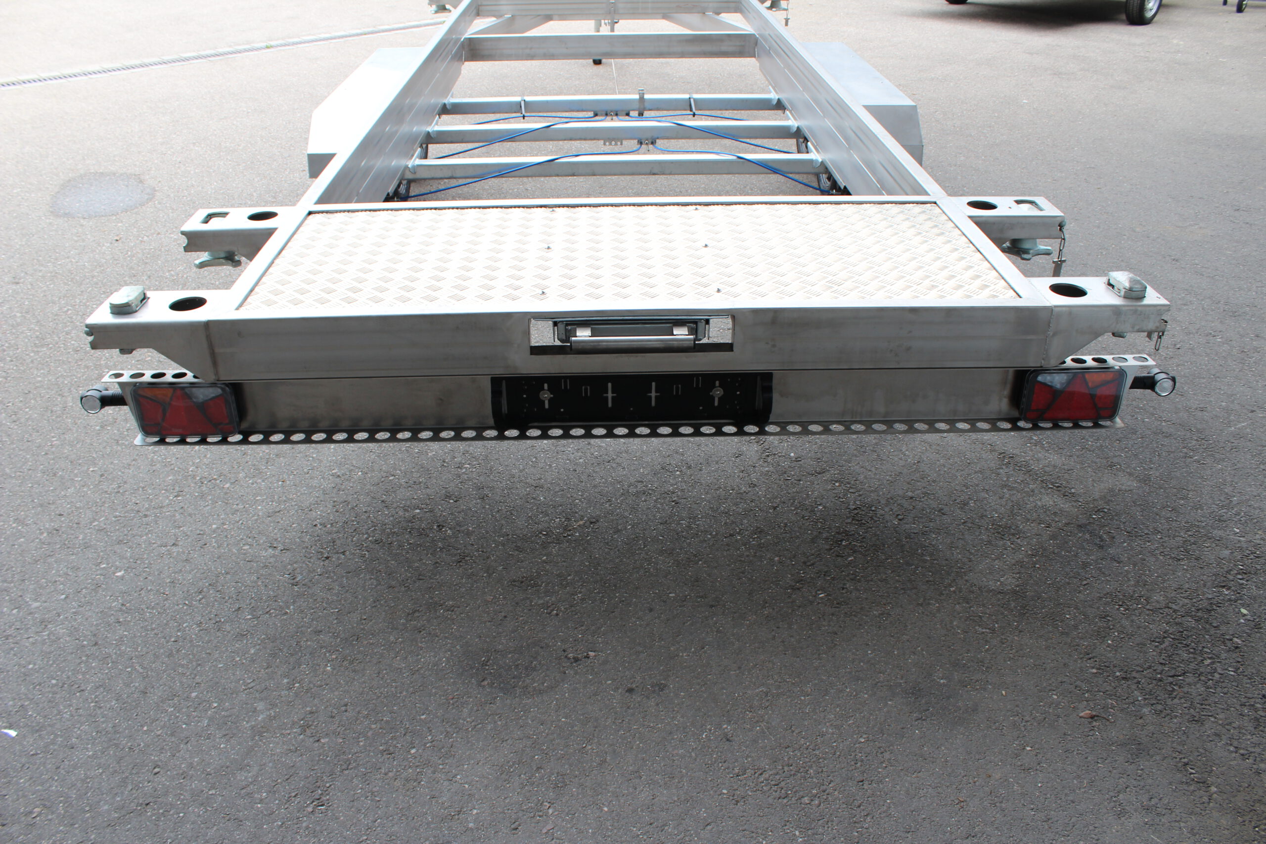 Anhänger aus Edelstahl zum Transport von Überseecontainern. Anhänger steht vor einem Hallentor. Anhängerfahrgestell ohne Bodenplatte für Containertransport.