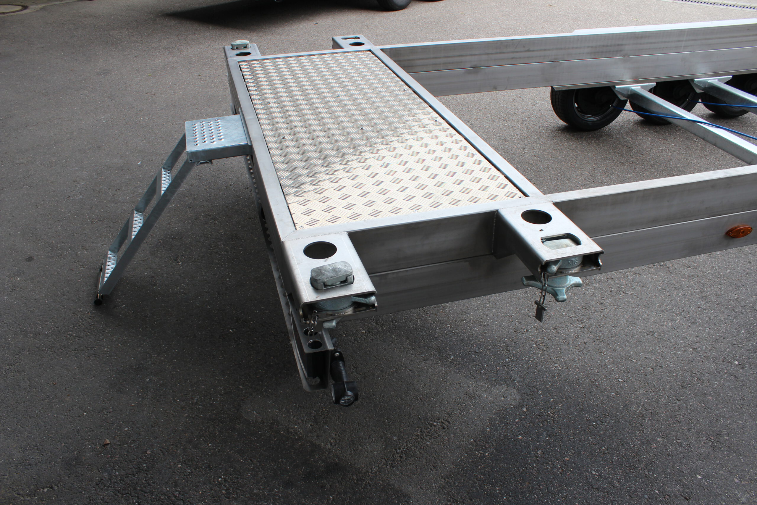 Anhänger aus Edelstahl zum Transport von Überseecontainern. Anhänger steht vor einem Hallentor. Anhängerfahrgestell ohne Bodenplatte für Containertransport.