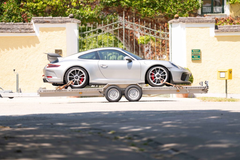 Tieflader Plattformanhänger Edelstahl mit Porsche GT3 vor einer Gelben Mauer