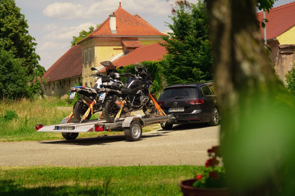 Silberner Absenkanhänger aus Aluminium mit zwei Motorrädern beladen hinter einem VW Passat