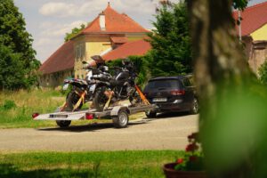 Silberner Absenkanhänger aus Aluminium mit zwei Motorrädern beladen hinter einem VW Passat