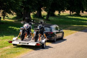 Silberner Absenkanhänger aus Aluminium mit zwei Motorrädern beladen hinter einem VW Passat