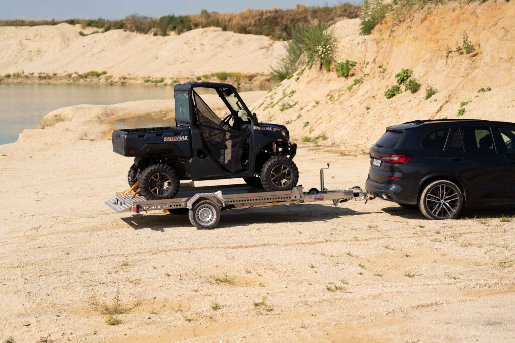 Absenkanhänger aus Aluminium mit schwarzem UTV beladen an einem BMW X5 in einer Kiesgrube