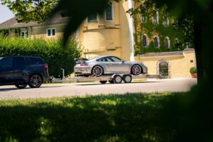 Edelstahl Tieflader Anhänger mit einem Porsche GT3 beladen vor einem gelben Haus