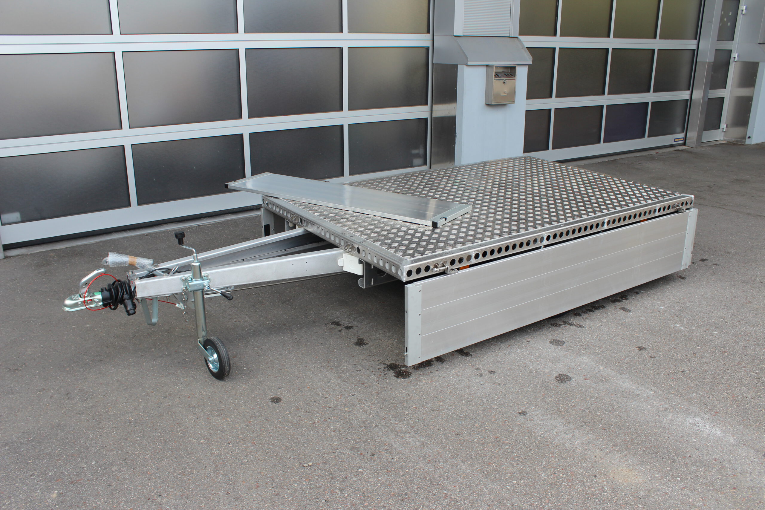 Aluminium Plattformanhänger mit Aluminium Bordwänden vor einem Hallentor