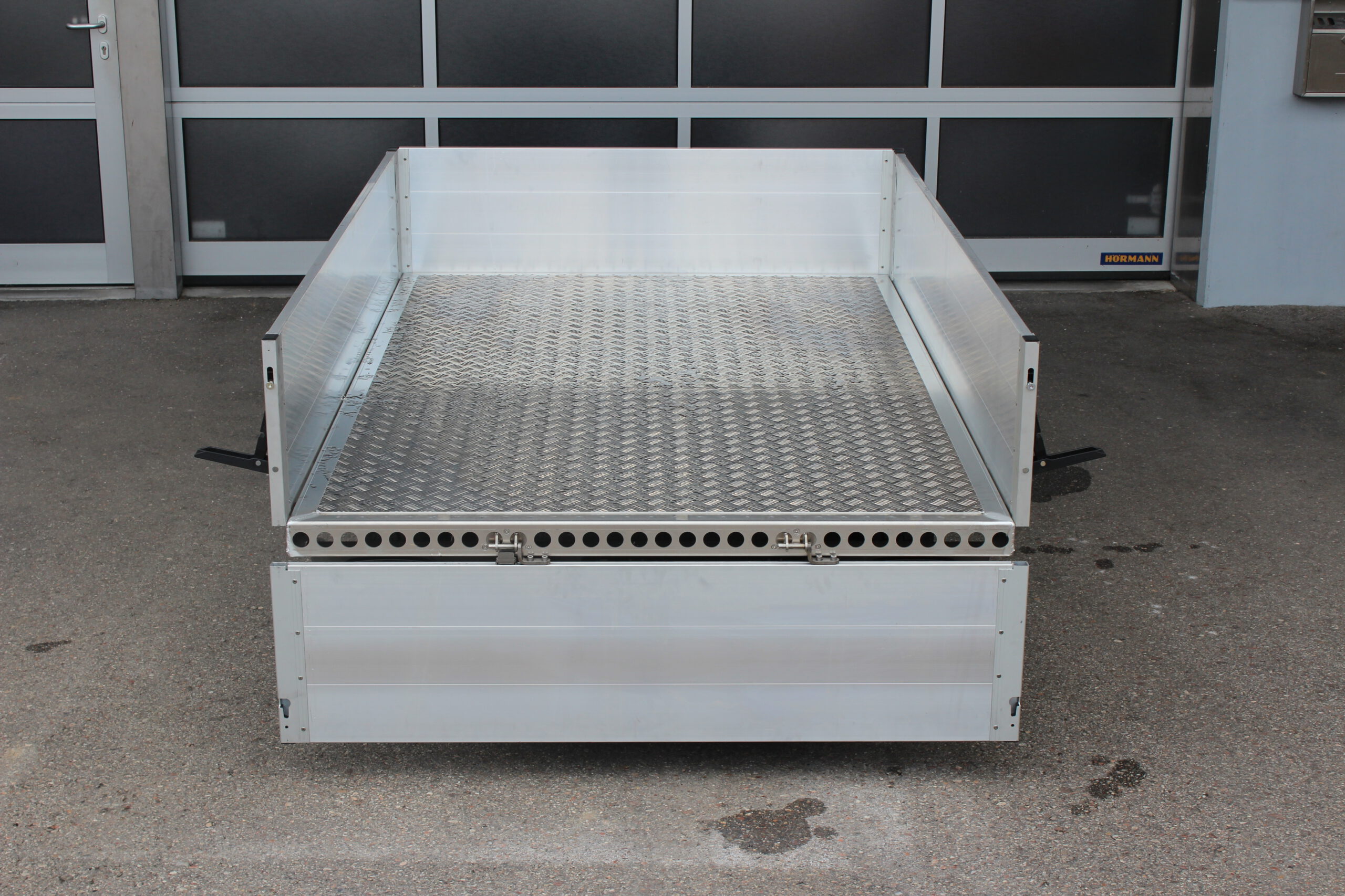 Aluminium Plattformanhänger mit Aluminium Bordwänden vor einem Hallentor