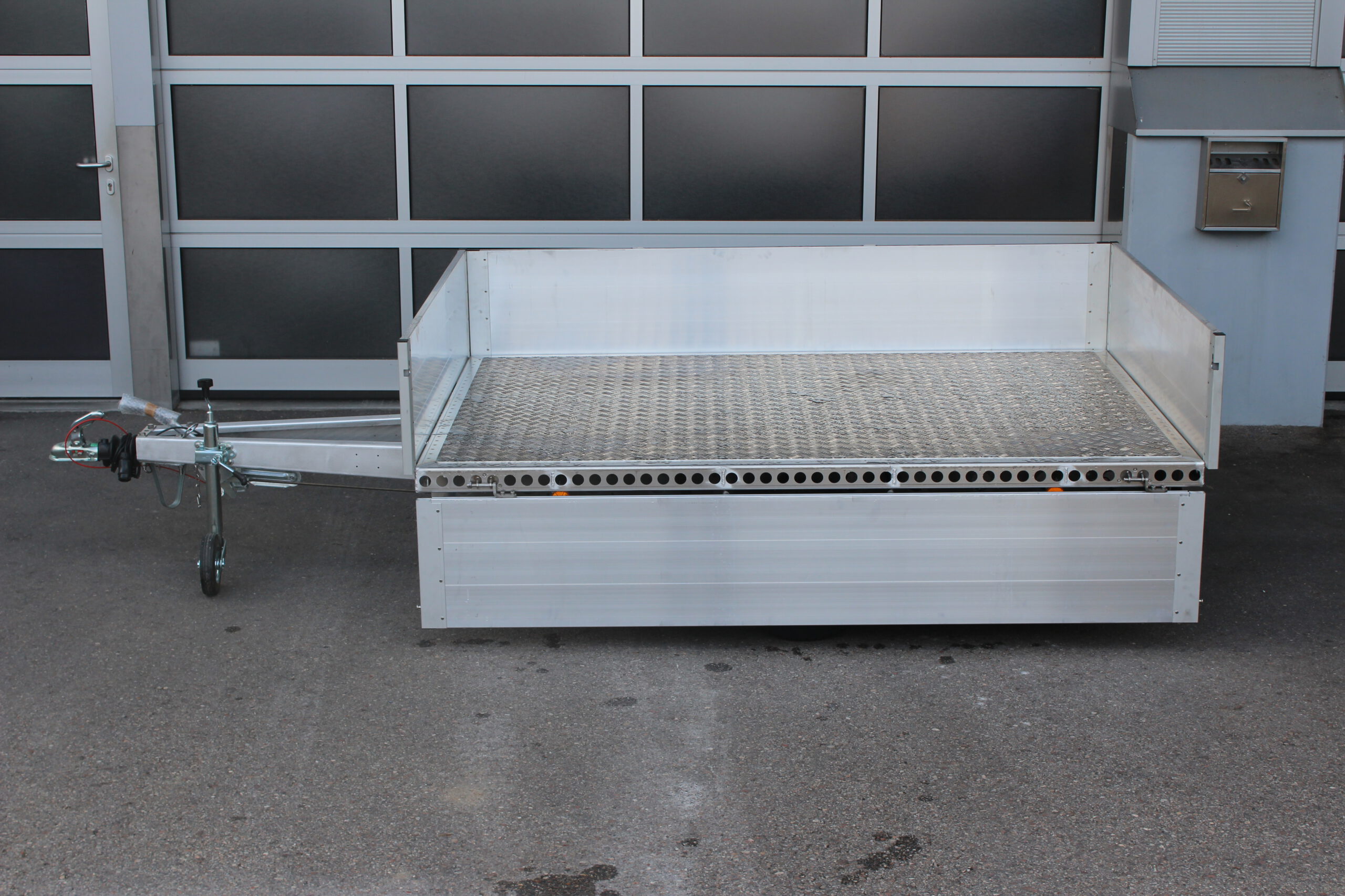 Aluminium Plattformanhänger mit Aluminium Bordwänden vor einem Hallentor